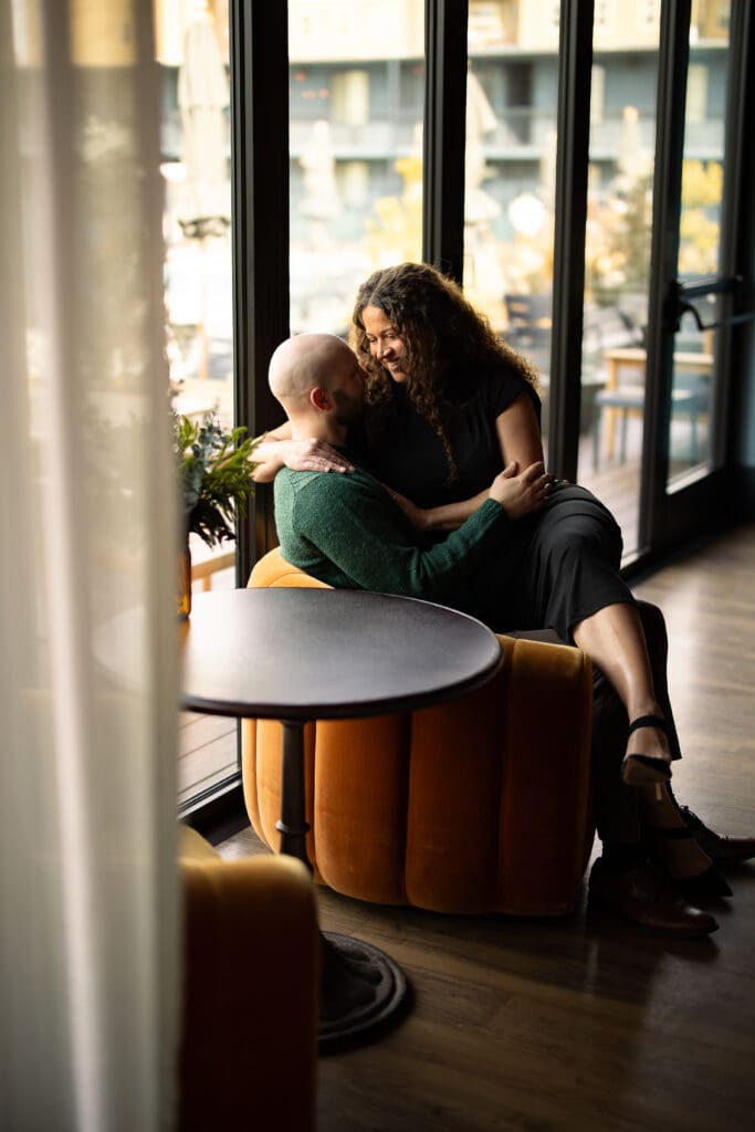 couples snuggles together on a chair by the window