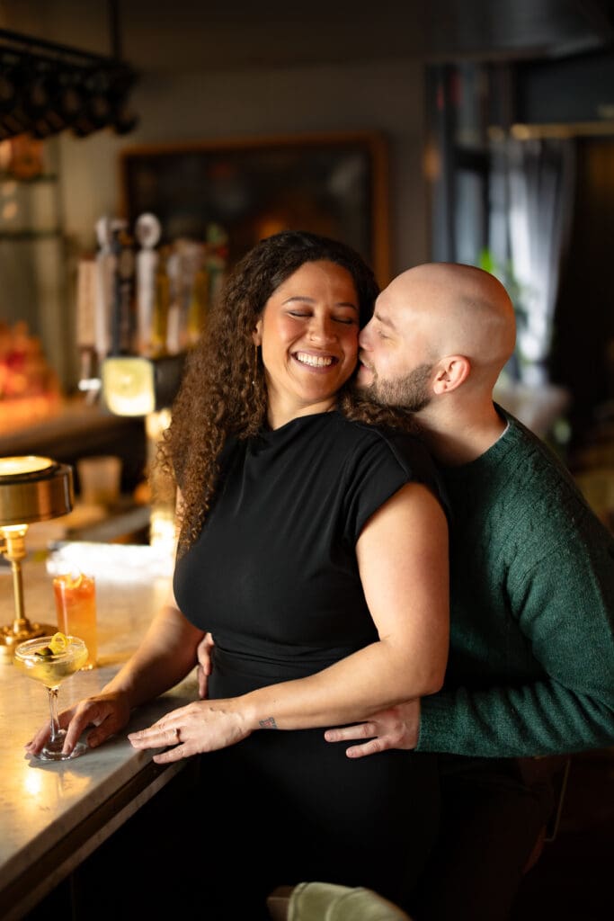 man stealing a kiss from his fiance at a cocktail bar