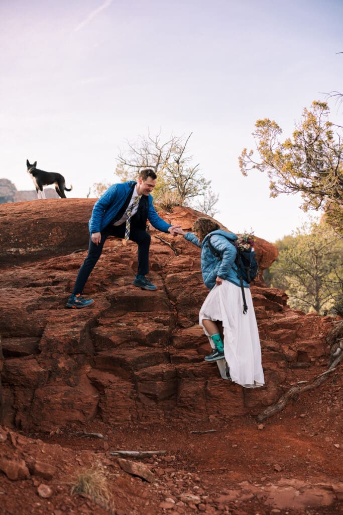 A bride and groom stay warm while hiking to their elopement location higher on the rocks. 