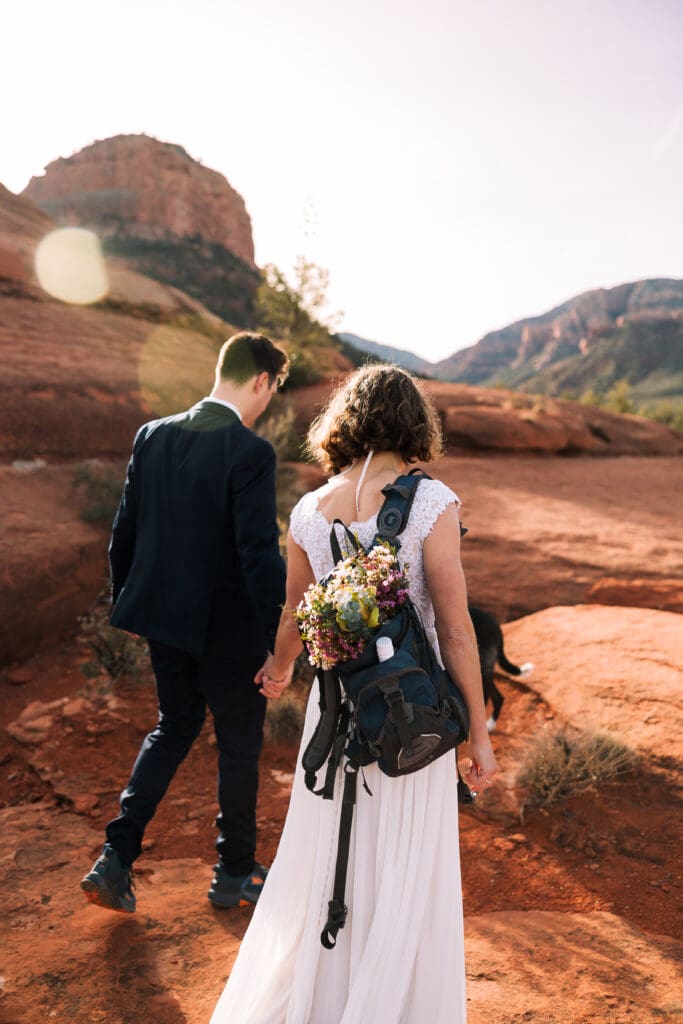 A bride carries her bouquet in her backpack as they hike to the elopement location.
