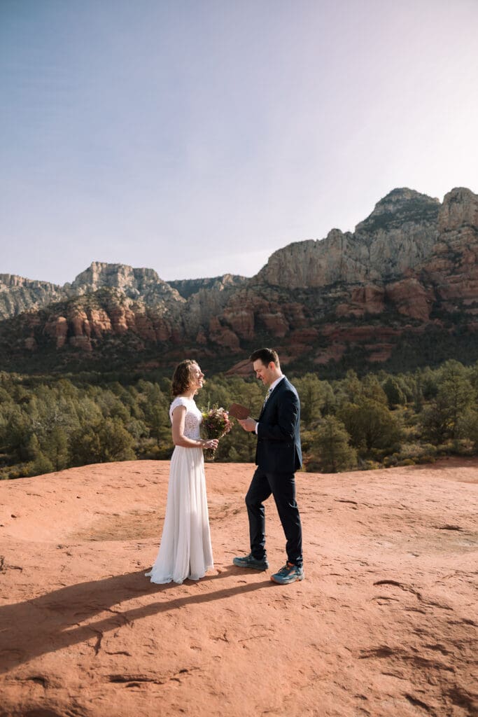 A couple shares vows in the sun with red rocks behind them.