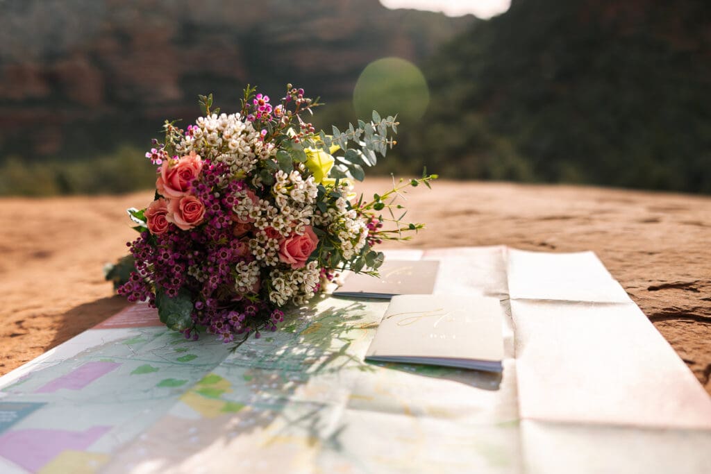 Elopement details such as bouquet, vow book and map are spread out on the red rocks of Sedona.