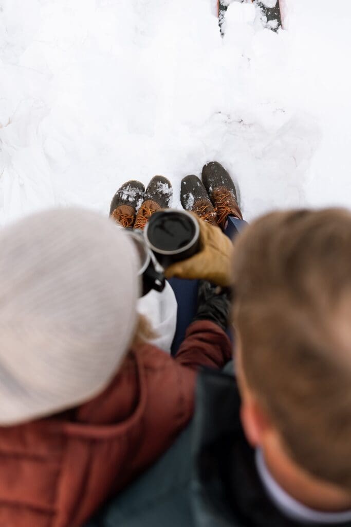 A bride and groom sit on a log as they hold each other and enjoy hot chocolate, perspective is from the top.