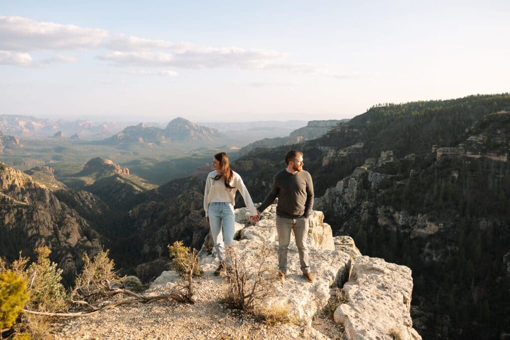 A couple stands side by side holding hands while looking away from each other with Capitol Butte aka Thunder Mountain in the distance. 