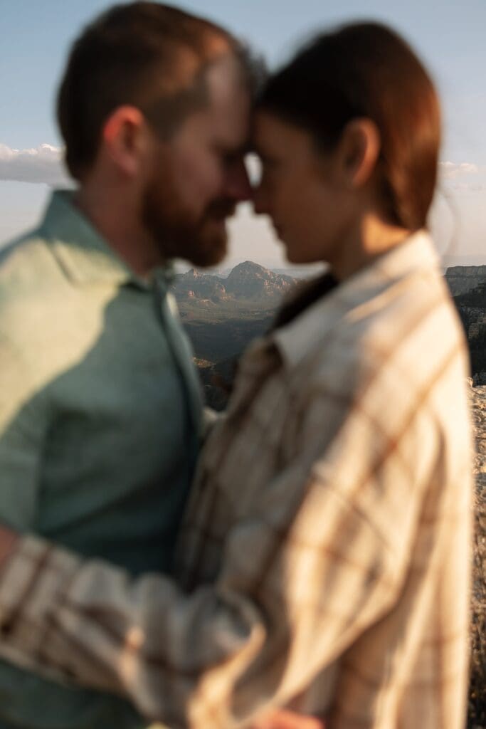 A couple stands facing each other creating a frame of Capitol Butte aka Thunder Mountain in the distance within the negative space of their bodies.