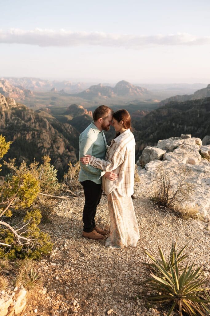 A couple stands facing each other on the Mogollon Rim overlooking Capitol Butte aka Thunder Mountain in the distance. 