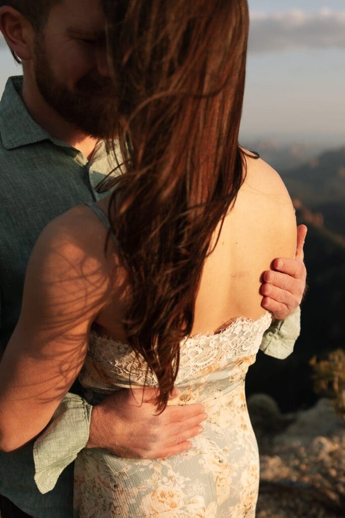 A man is gently holding his partner with the focus being his band on her back with glowing light touching her skin.