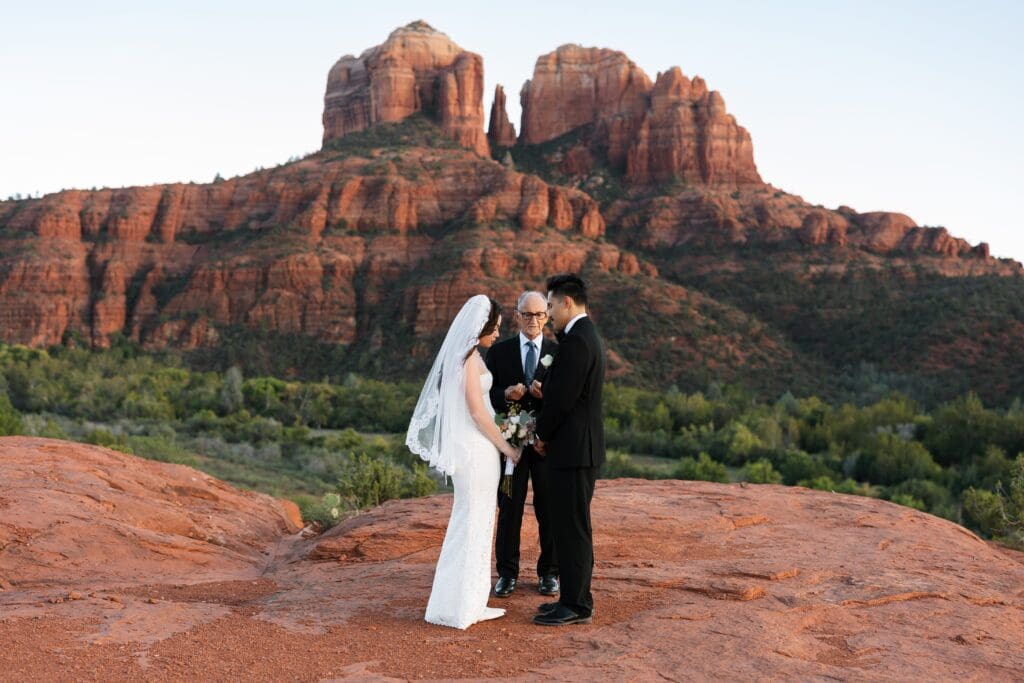 Sedona elopement at Secret Slickrock. Bride and groom exchanging vows with an officiant and the iconic red rock landscape behind them.