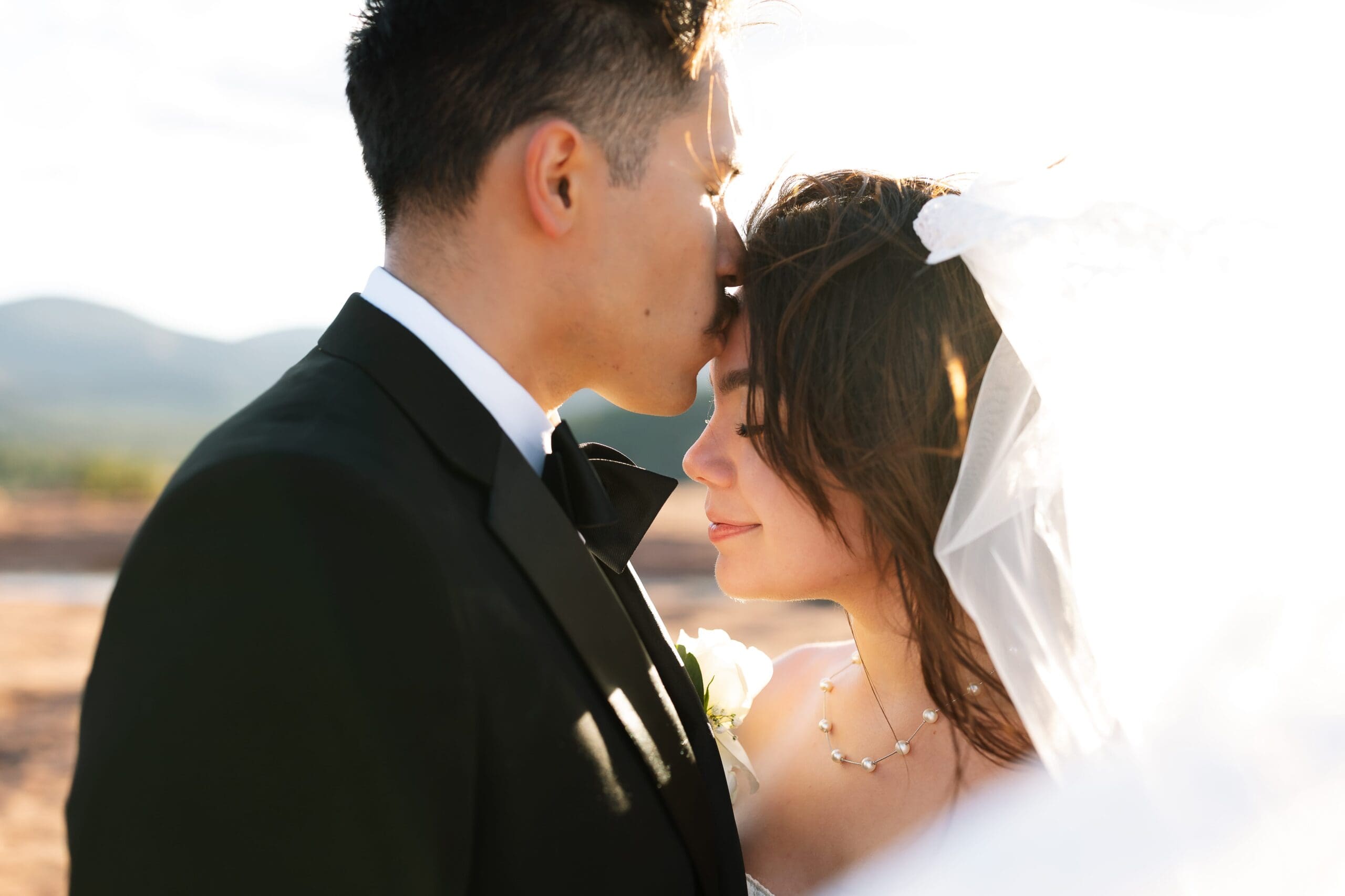 a groom kisses his bride on the forehead after a secret slickrock elopement at sunset.