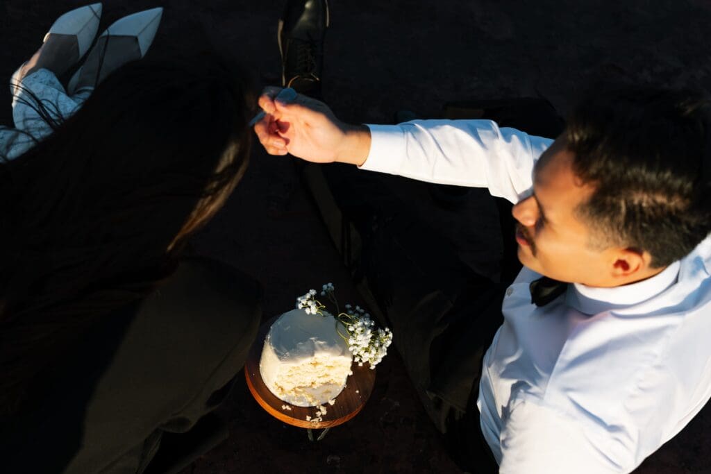 a groom feeds his bride a piece of cake as they celebrate their recent marriage. 