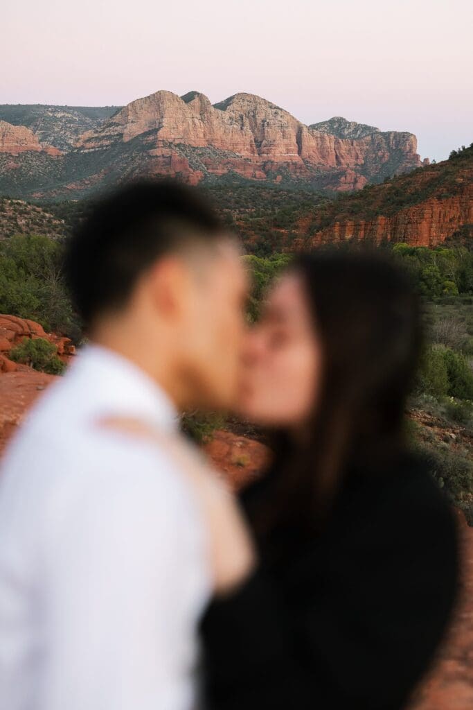 A bridge and groom kiss with the soft sunset light hits the red rocks in the background at an October secret slickrock elopement.