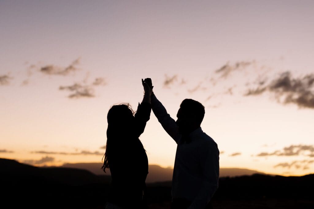 A silhouette of a bride and groom dance at sunset at secret slickrock.