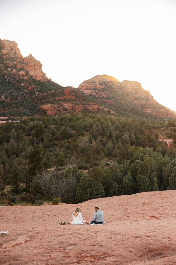 Elopement couple sitting on cliff edge at sunset in Sedona Arizona having a picnic.