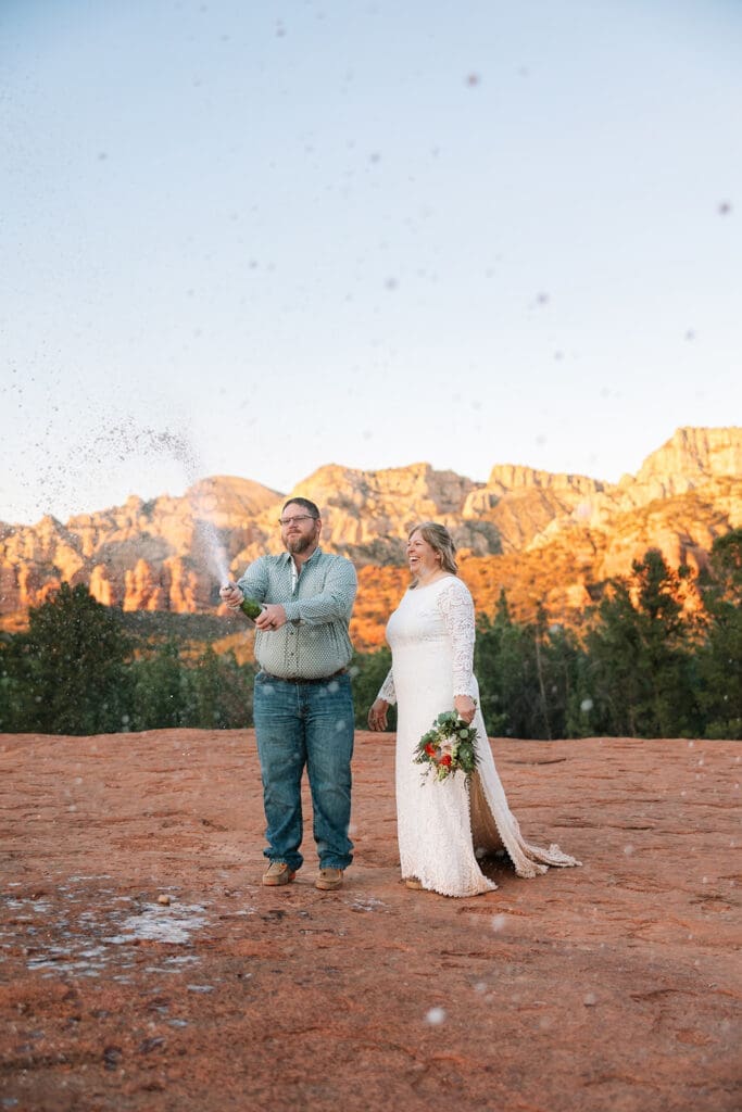 Bride and groom popping champagne on Submarine Rock during Sedona adventure elopement