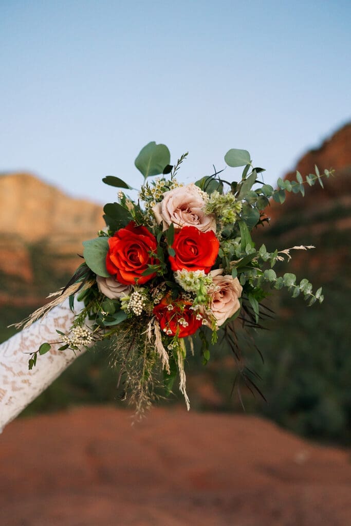 A bride holds her bouquet against the red rocks of Sedona at sunset.