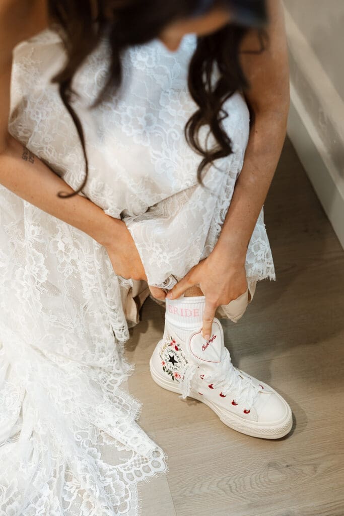 Close-up of a bride lifting her lace wedding dress to reveal custom embroidered high-top canvas sneakers for her Sedona elopement.