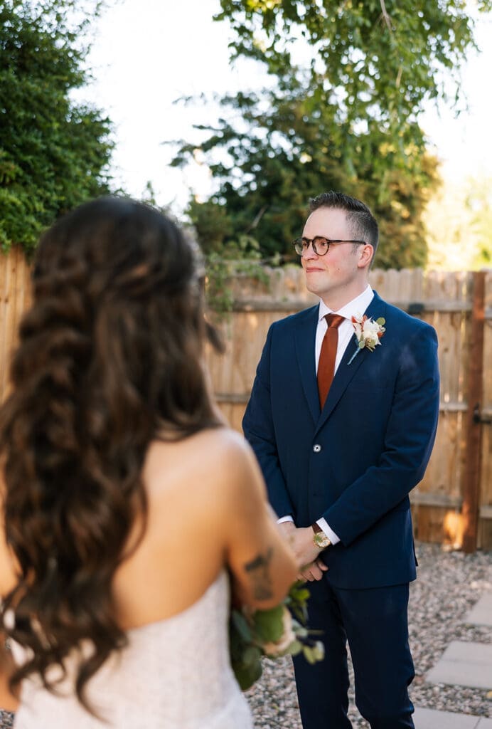 Candid back-view of a bride with half-up wavy hair looking at her groom during an emotional first look moment.