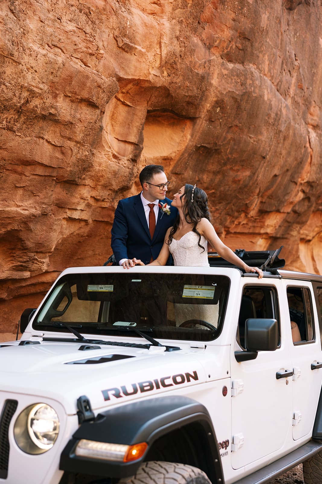 Eloping bride and groom kissing while standing through the sun roof in their white Jeep Wrangler in the Sedona red rock desert.