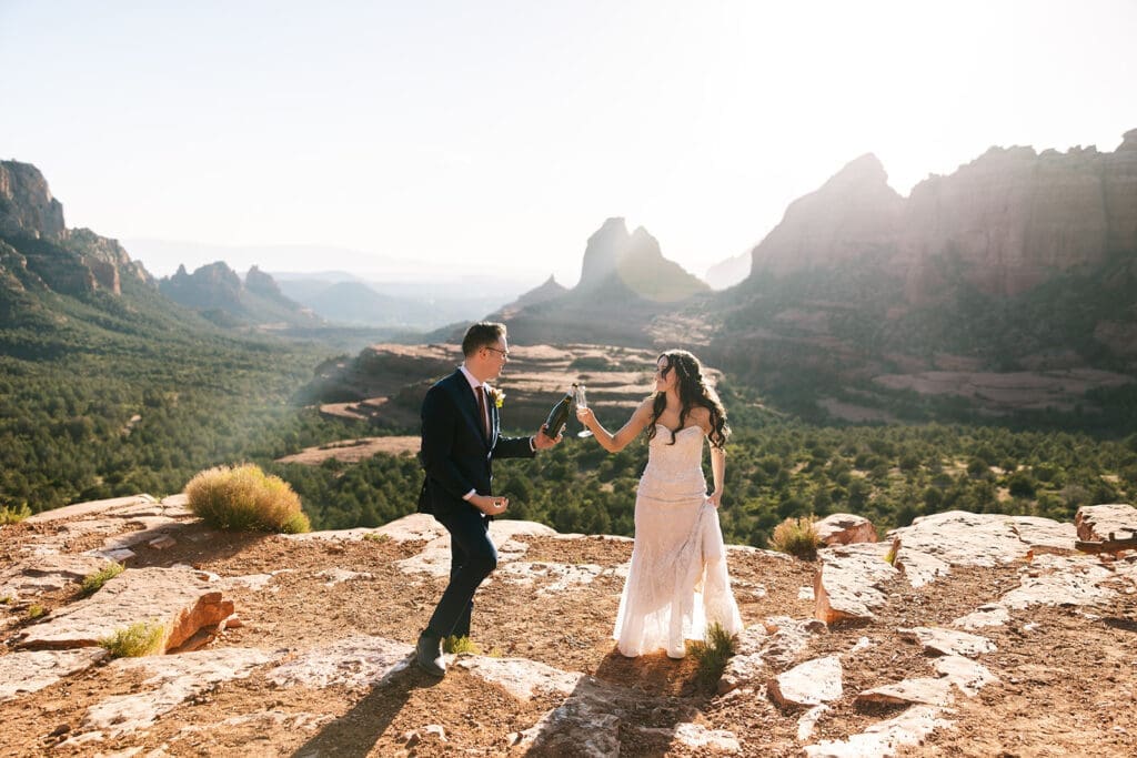 Eloping bride and groom popping champagne together at Merry Go Round Rock during their off-roading Sedona elopement.