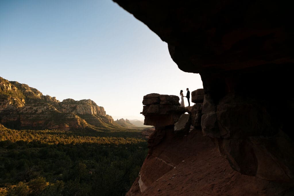 Silhouetted photo of the bride and groom standing underneath the natural rock arch overhang at Merry Go Round Rock in Sedona.