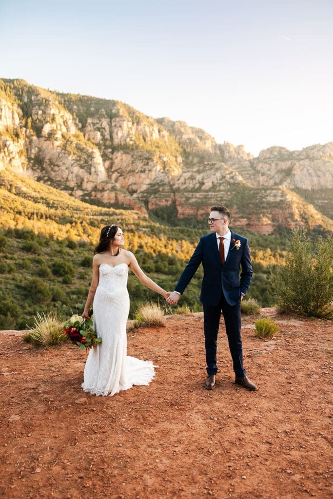 Eloping couple standing near the edge of a cliff enjoying the expansive red rock landscape during golden hour in Sedona.