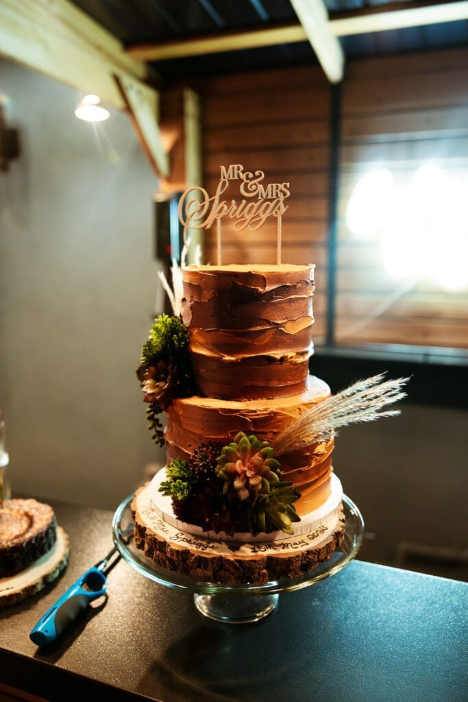 Close-up of a rustic, multi-tiered wedding cake with a custom 'Mr. & Mrs.' topper at a private reception.