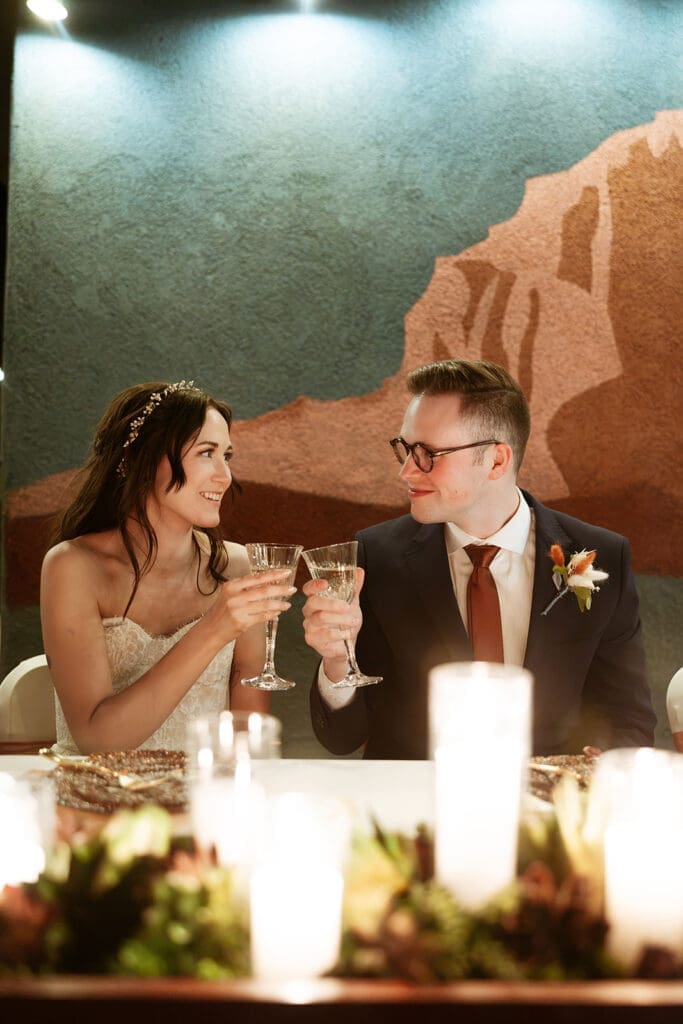 Candid photo of the bride and groom smiling and sitting together at their indoor wedding reception dinner table.