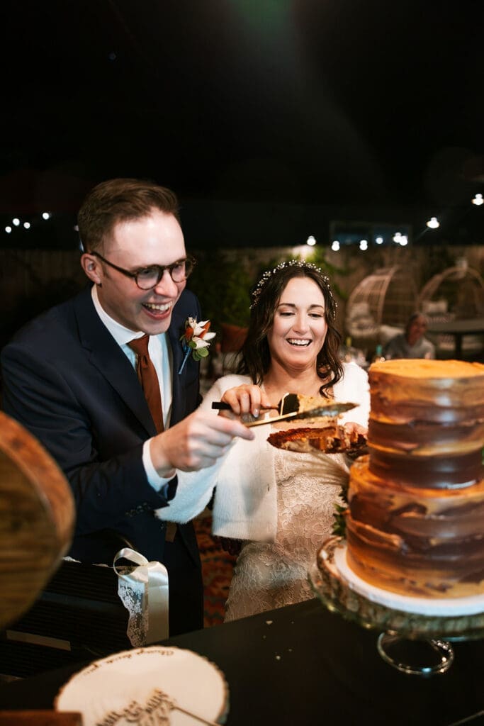 Close-up shot of the groom and bride using a cake knife and server to cut the first slice of their wedding cake.