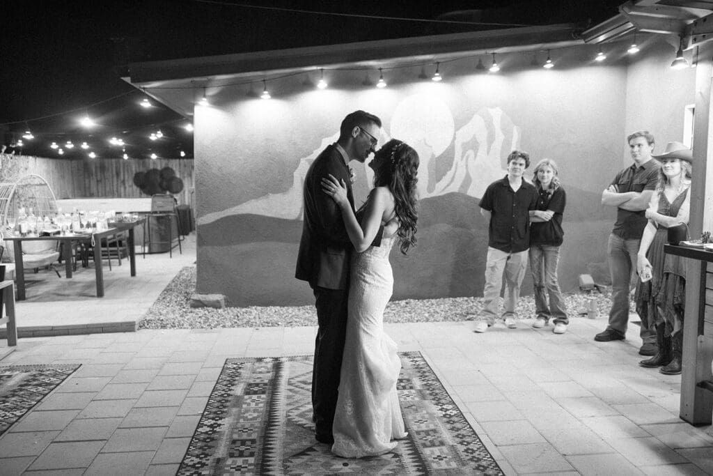 Artistic vertical shot of the bride and groom sharing their first dance as husband and wife under warm bistro lights.