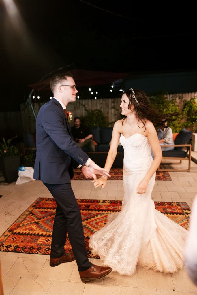 Wide-angle view of the newlyweds dancing on a rug, framed by a scenic wall mural and celebrating with guests.