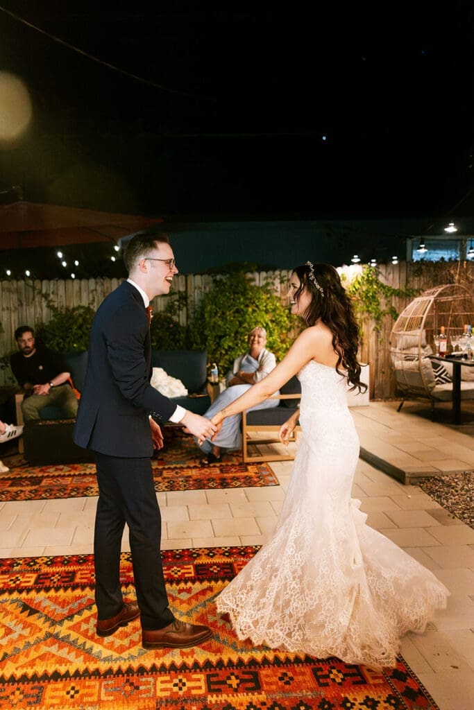 Wide-angle view of the bride and groom holding hands and dancing outdoors at night under glowing bistro lights at their Sedona reception.