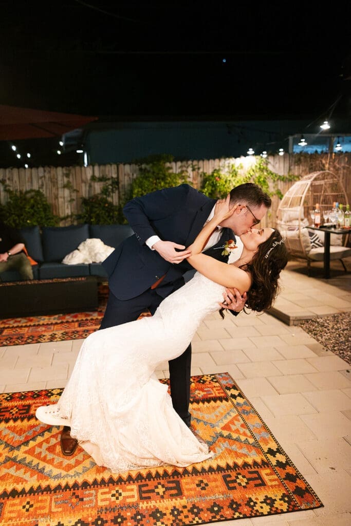 The groom dipping the bride low for a romantic kiss during their first dance on a rug at an outdoor reception.