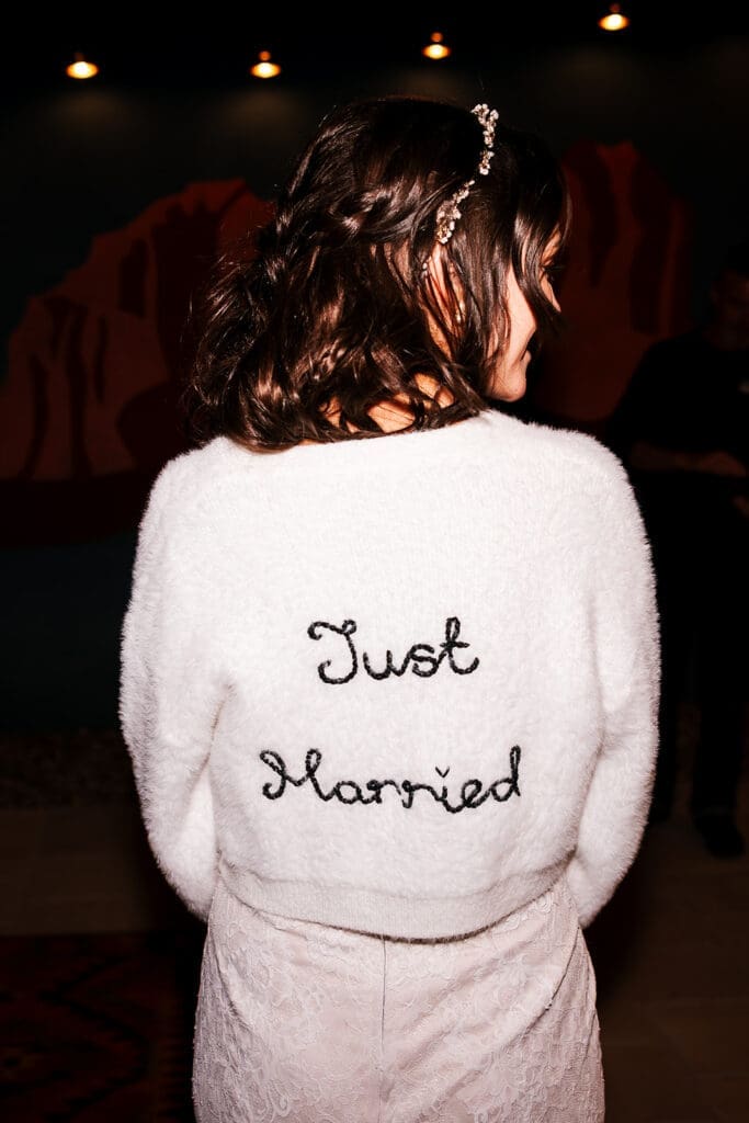 Back view of the bride wearing a cozy, white fuzzy jacket embroidered with 'Just Married' on the back during her Sedona elopement.