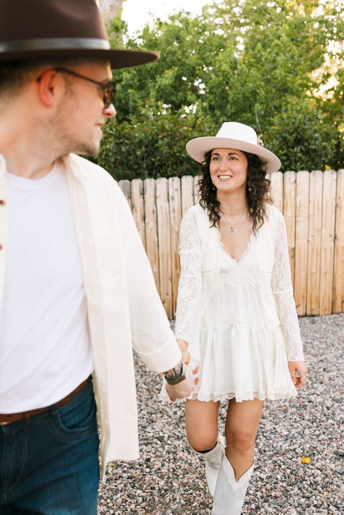 The groom in a white button-up shirt smiling and walking hand-in-hand with his bride outside during their mobile hat bar event in Sedona.