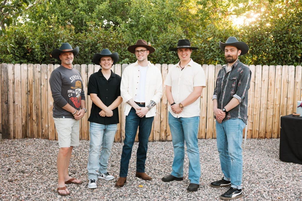 Groom and groomsmen wearing custom hats smiling and posing together outside ahead of the elopement ceremony.