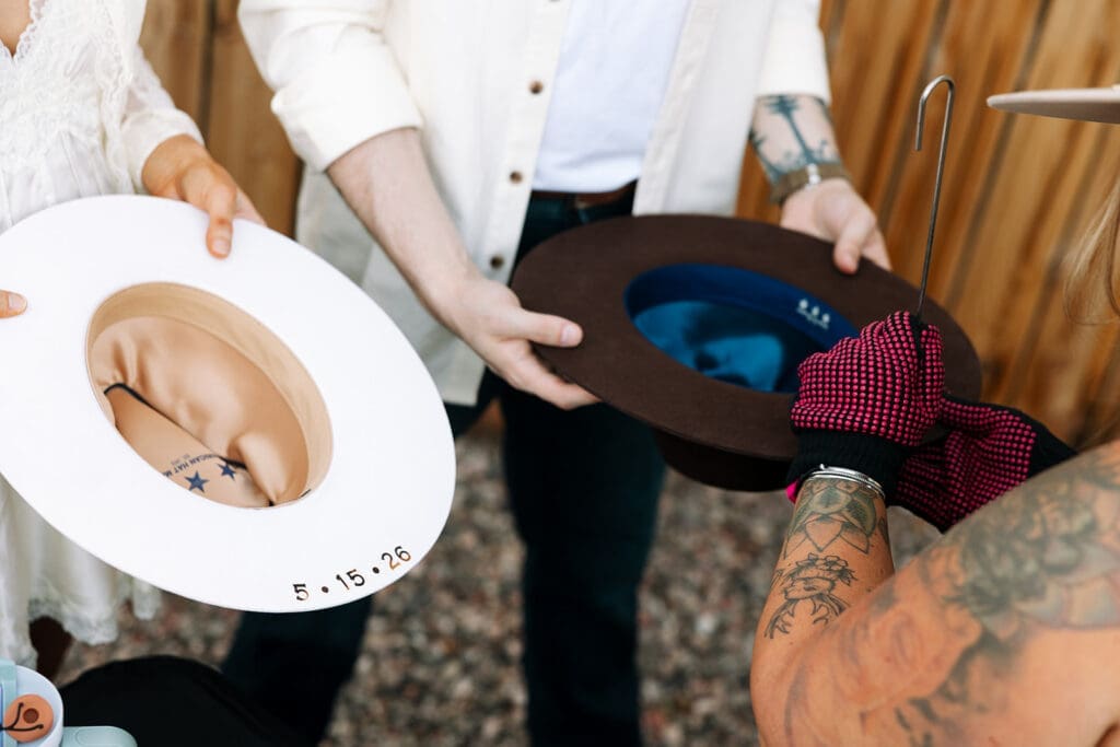 Close-up shot of hands holding two customized cowboy hats showing the detailed brim branding and inside date signatures.