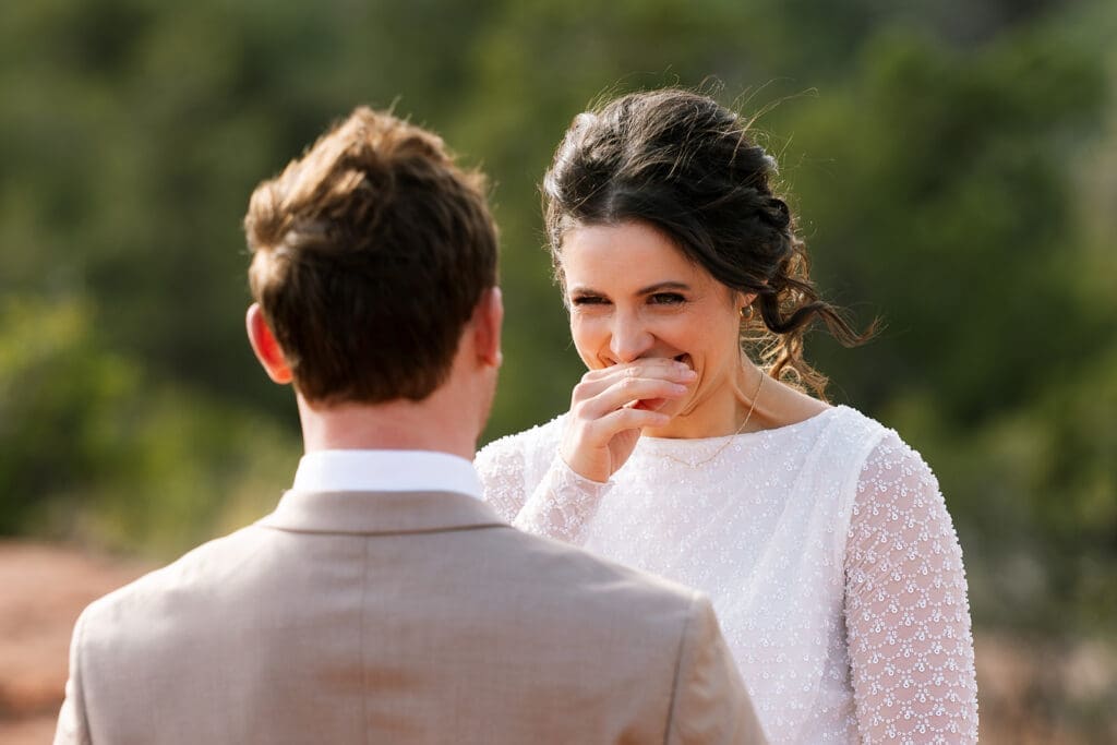 Close-up candid photo of the bride smiling emotionally with her hand to her mouth during her intimate Sedona elopement ceremony.