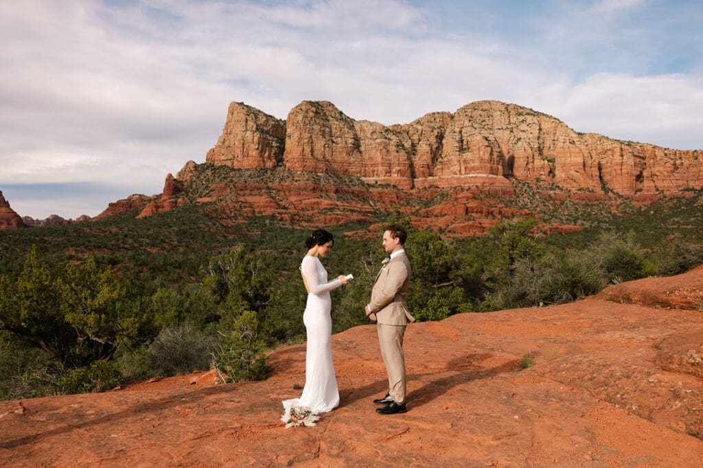 Bride reading her vows to the groom against the towering backdrop of Baby Bell Rock during a Sedona sunset elopement.