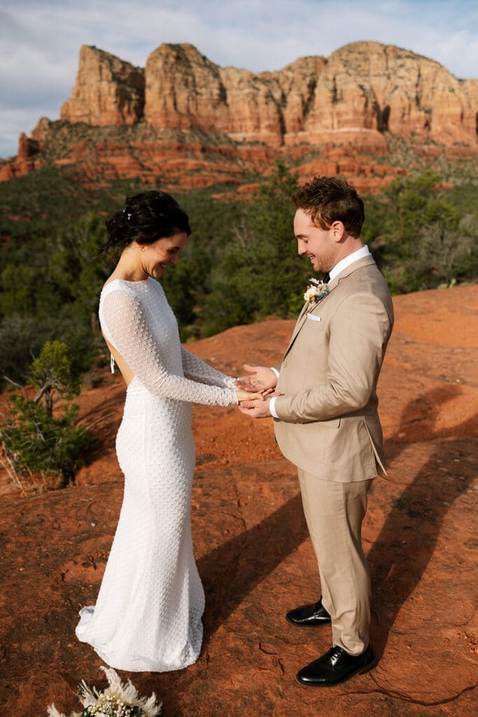 Bride and groom holding hands and smiling at each other during an intimate red rock elopement ceremony in Sedona.