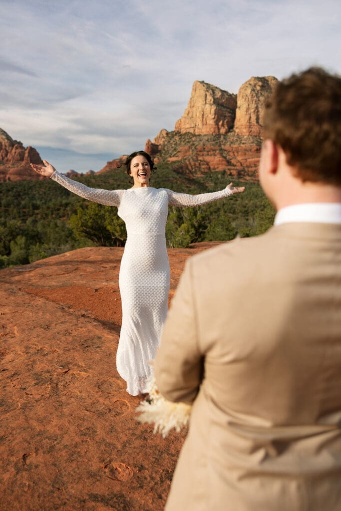 Bride with her arms outstretched happily celebrating after getting married at Baby Bell Rock in Sedona.