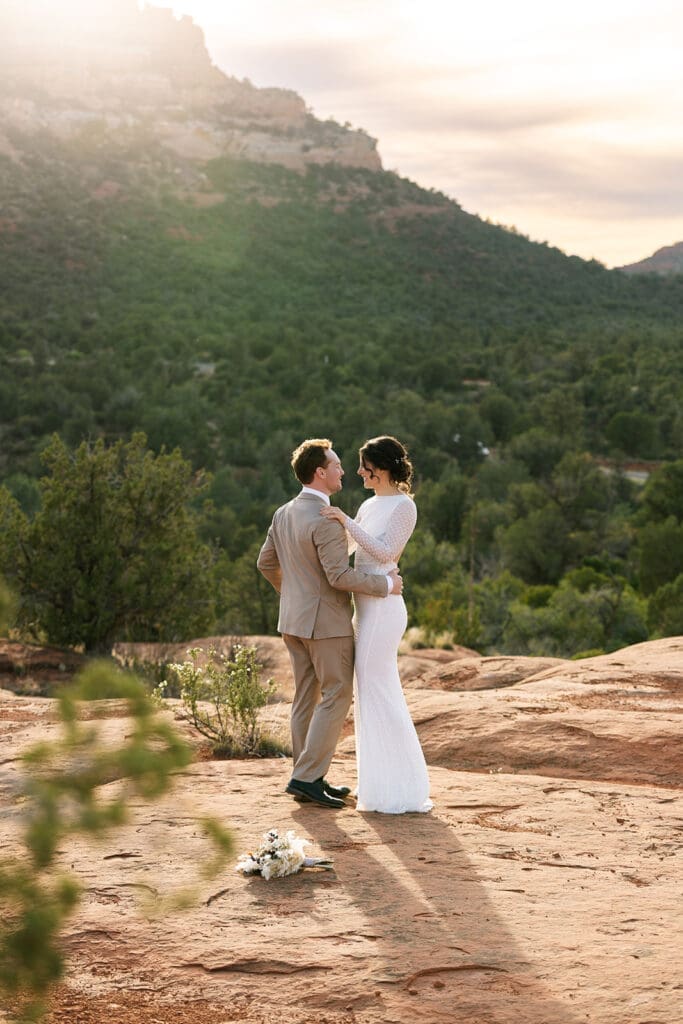 Wide-angle portrait of the bride and groom embracing on a red rock plateau in Sedona during golden hour.