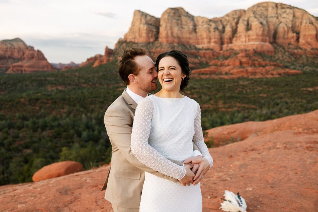 Close-up candid shot of the groom smiling and leaning in close to the bride as she laughs joyfully during their desert elopement.