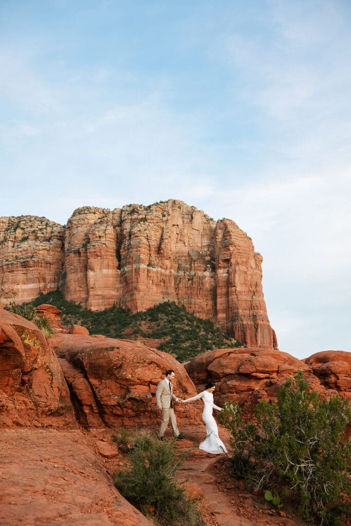 Expansive landscape photo showing the eloping couple walking down a red rock trail framed by towering canyon walls in Sedona.